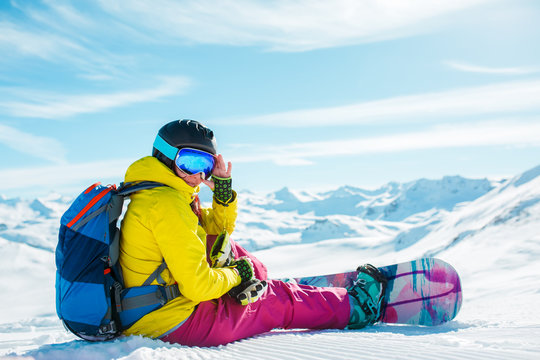 Photo of woman in helmet with backpack sitting on snow with snowboard