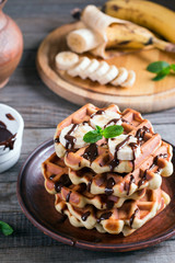 Waffles with chocolate syrup and banana slice on a plate on a wooden background