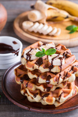 Belgian waffles with chocolate syrup and banana slice on a plate on a wooden background