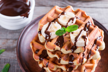 Belgian waffles with chocolate syrup and banana slice on a plate on a wooden background