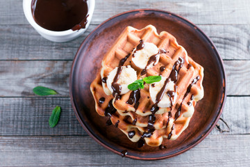 Wafers with banana and chocolate sauce on a wooden background.