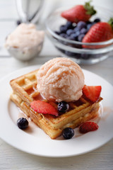 Waffle with scoop of strawberry ice cream, blueberry, strawberry and sauce.