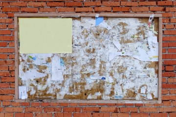 old wooden Billboard frame with blank yellow paper sheet on red brick wall.