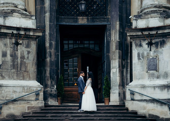 Charming young couple of newlyweds is softly holding hands and looking at each other while standing...