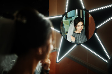 Fabulous bride looking at star-shaped mirror in makeup salon before the wedding.