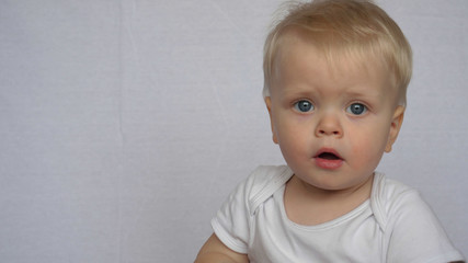 Naklejka premium Portrait of a beautiful little baby (boy), looks into the camera, blond, light-haired, blue eyes, white background. Concept: babies, fair skin, beautiful children.