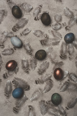 top view of painted and golden eggs on concrete surface with feathers