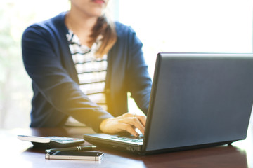 Selective focus Young business woman working on laptop computer. Female hands on the keyboard Office workplace with calculator and smartphone on wood table background.