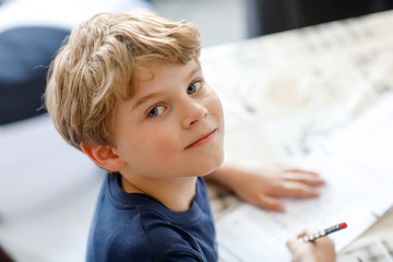 Happy smiling kid boy at home making homework writing letters with colorful pens