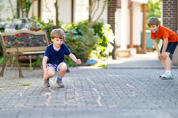 Two little school and preschool kids boys playing hopscotch on playground