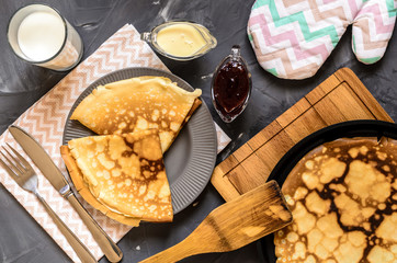 Top view of the Russian dish pancakes, milk, jam, white chocolate, towel, potholder, knife and fork.