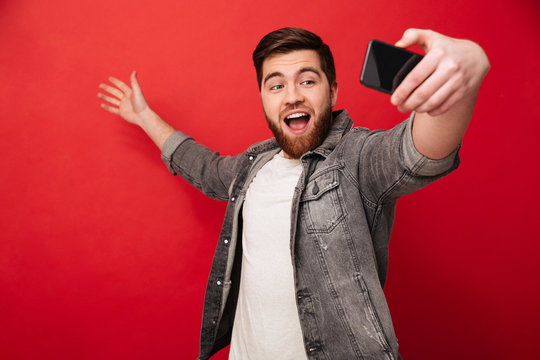 Happy bearded man making selfie on smartphone and presents copyspace