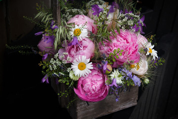 Flower arrangement, bouquet with pink peony, chamomile and green plants in wooden basket on dark background