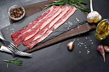 Bacon rashers with rosemary, garlic and olive oil isolated on black background. Top view.