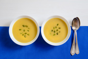 Soup of pumpkin and sunflower seeds in a white plate with silver spoons on a bright background. The concept of healthy eating, weight loss, diet, health care