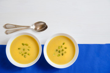 Soup of pumpkin and sunflower seeds in a white plate with silver spoons on a bright background. The concept of healthy eating, weight loss, diet, health care