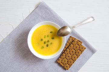 Soup of pumpkin and sunflower seeds in a white plate with a silver spoon and bread on a linen napkin. The concept of healthy eating, weight loss, diet, health care