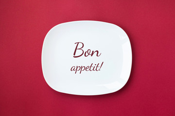 White plate with inscription Bon appetit on red background.
