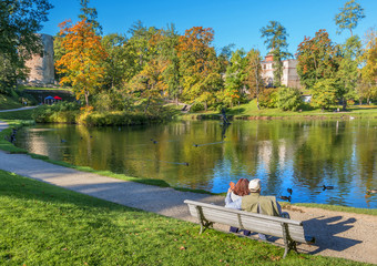Happy couple of seniors are resting on the wooden bench in a public old park and  looking at the distance of city lake