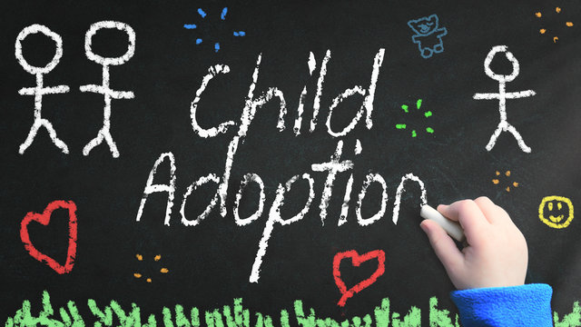 Kid's hand writing Child Adoption on a blackboard with a chalk and some drawings
