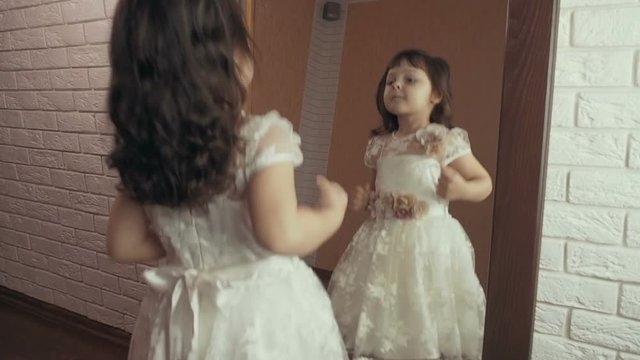 Funny child at the mirror. Beautiful little girl is jumping near the mirror.