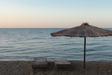 Straw parasol and sunbed on pebble beach