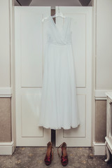 Suknia ślubna wisząca na białej szafie oraz buty. - obrazy, fototapety, plakaty