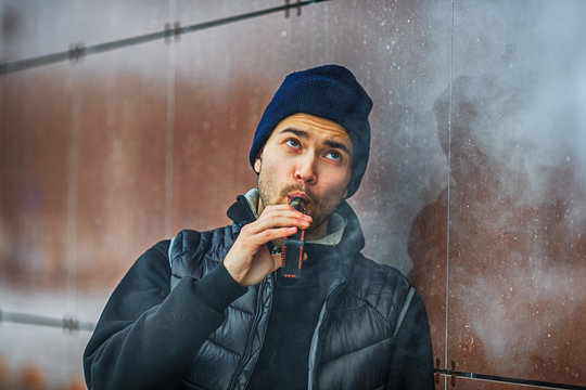 Vape man. Portrait of a handsome young white guy vaping an electronic cigarette opposite the futuristic modern background. Lifestyle. Close up.
