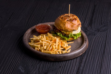 Appetizing burger, sauce and french fries on clay plate, wooden background