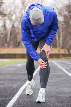Shot of a young runner holding his injured knee while running.