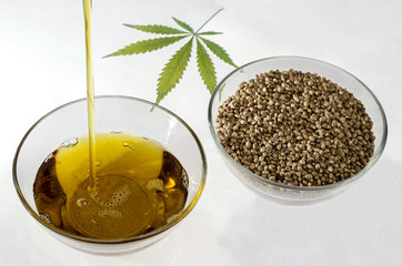 A stream of flowing hempseed oil and hemp seeds in a round glass bowl..