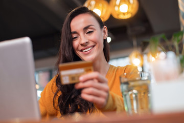 Payment everywhere. Low angle of sincere pleasant satisfied woman looking at credit card while...