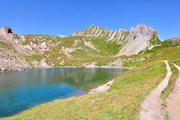Naklejka na ściany i meble footpath along a lake in rocky peaks in alpine mountain in summer 