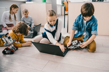 kids programming robots with laptops while sitting on floor, stem education concept