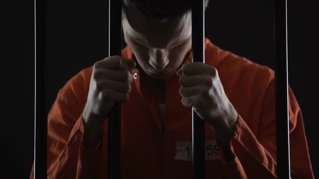 Thief in jail feeling sincere regret of crime, holding prison bars in desperate