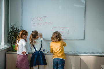 rear view of children writing and drawing robot education signs on whiteboard