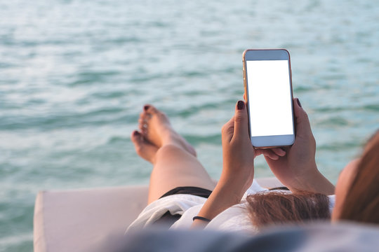 Mockup image of a woman using white mobile phone with blank desktop screen while lying by the sea