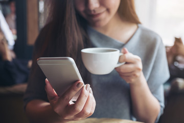 Closeup image of a beautiful Asian woman holding and using smartphone while drinking coffee in cafe