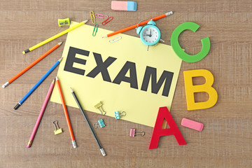 Paper with word EXAM and stationery on wooden background