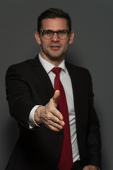 Blurred Businessman wearing formal suit and glasses holds out his hand for a handshake on gray background