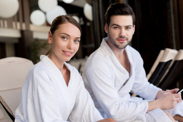 beautiful young couple in bathrobes smiling at camera in spa center