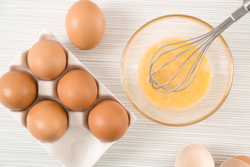 Beating up chicken eggs with whisk in glass bowl on table