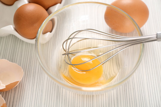 Beating up chicken eggs with whisk in glass bowl on table