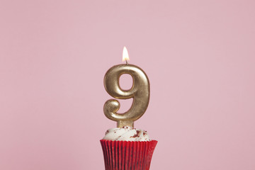 Number 9 gold candle in a cupcake against a pastel pink background