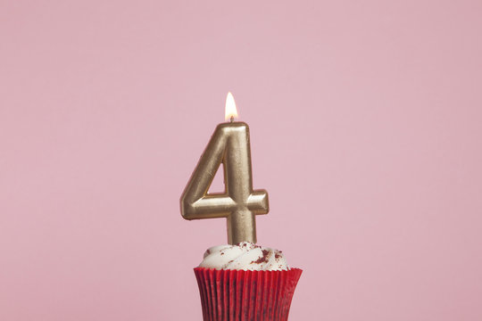 Number 4 gold candle in a cupcake against a pastel pink background