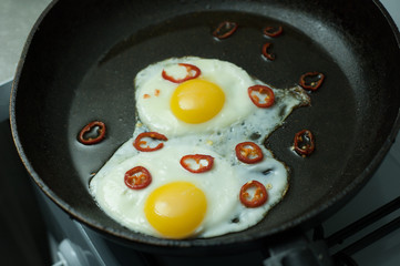 Two fried eggs with chili pepper in a skillet.