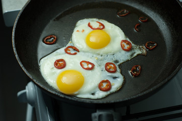 Two fried eggs with chili pepper in a skillet.