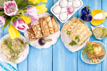 Thin pancakes for the spring Russian holiday with different fillings. Traditional food. Wessing breakfast. Easter and carnival. A bouquet of bright tulips. Blue background. Card. Place for text.