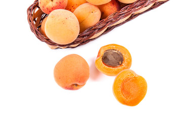 Several of harvested apricots in basket with whole and halved apricots on white background..