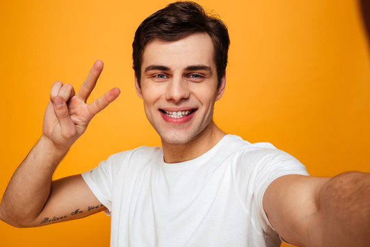 Smiling man in t-shirt making selfie while showing peace gesture